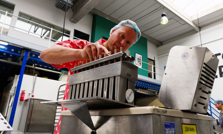 Man in roze shirt en blauw haarnetje werk met een machine dat ijsjes maakt