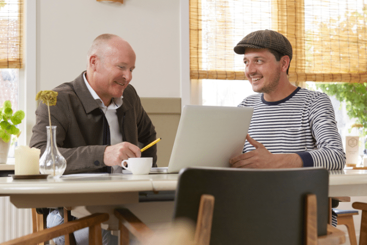 Twee mannen zitten aan een huistafel met laptop en praten