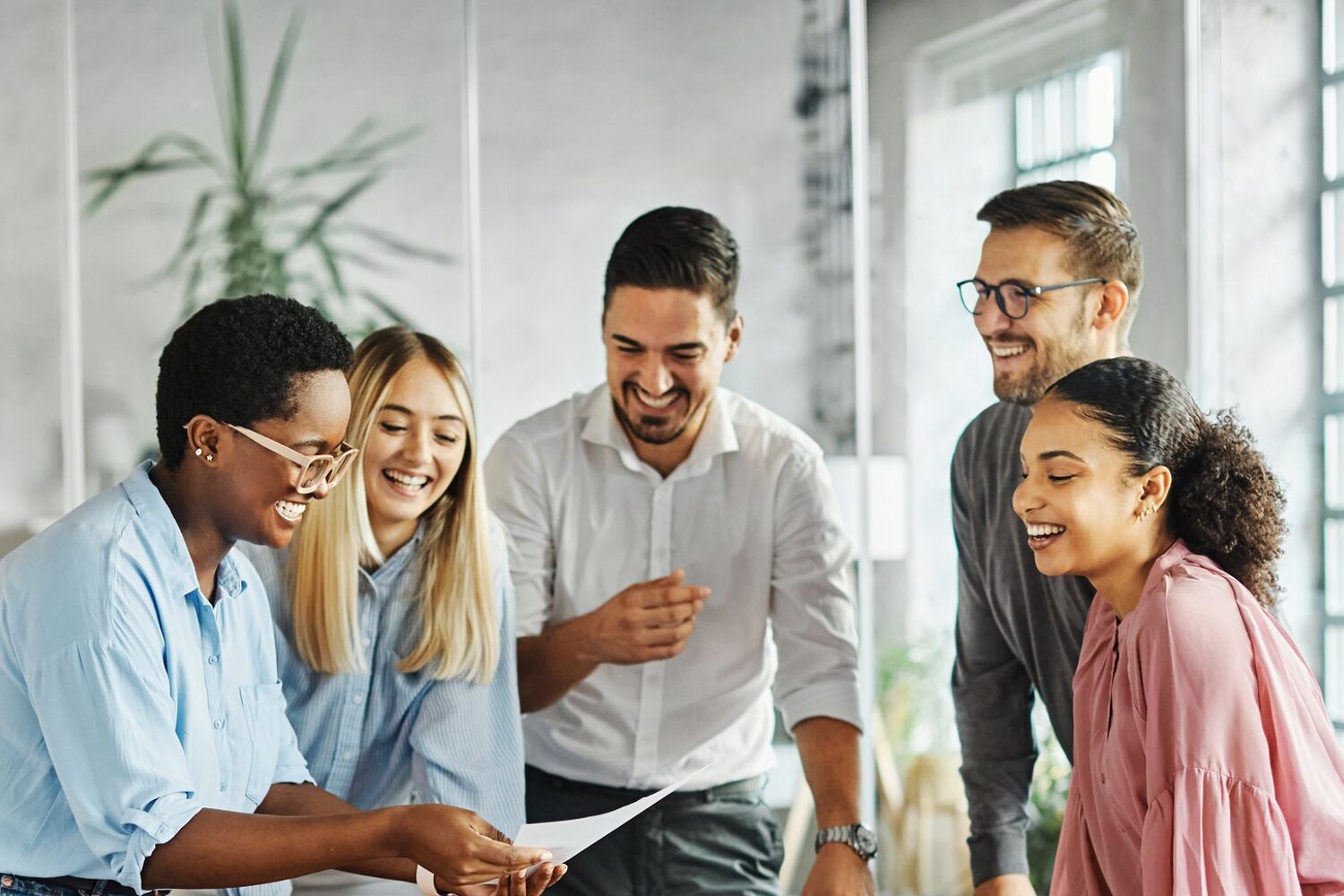 Een groep mensen staan naast een tafel en lachen, ze kijken naar een document. 