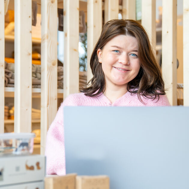 Vrouw zit lachend achter de laptop en kijkt in de camera