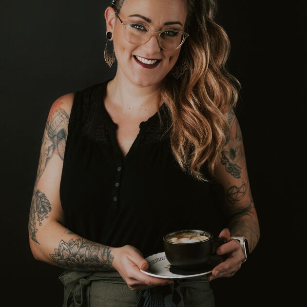 Vrouw met een bril en koffie in haar handen voor een zwarte achtergrond. 