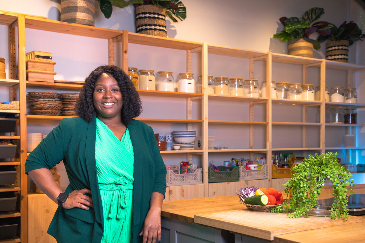 vrouw staat trots in haar eigen kookstudio en draagt een groene jumpsuit