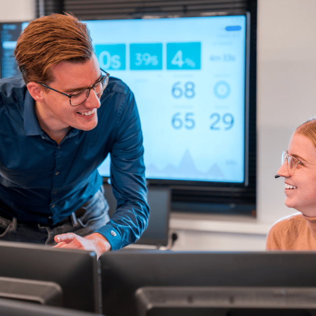 Man in blauw shirt praat tegen vrouw achter computer