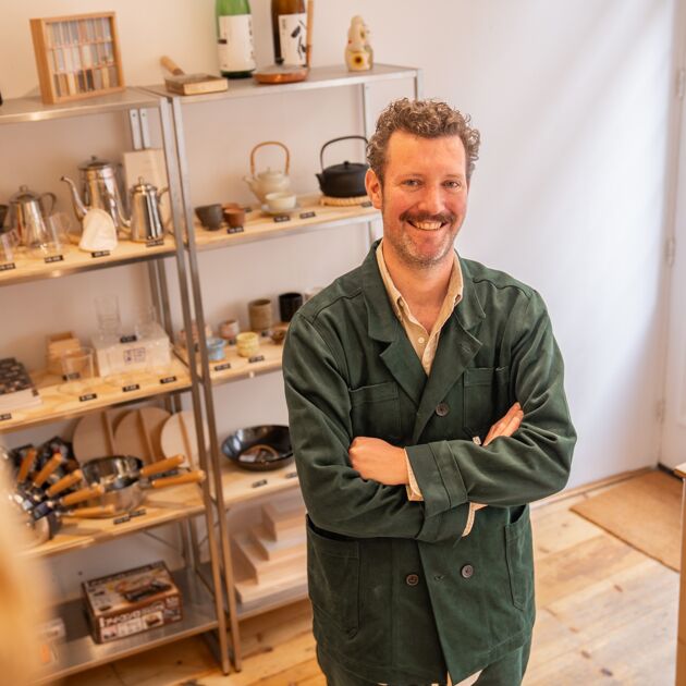 Een lachende man met een groene jas staat in een winkel. 