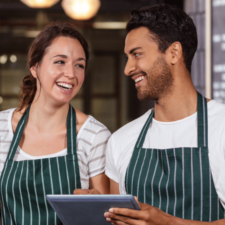 Man en vrouw met een schort om kijken lachend naar elkaar. 