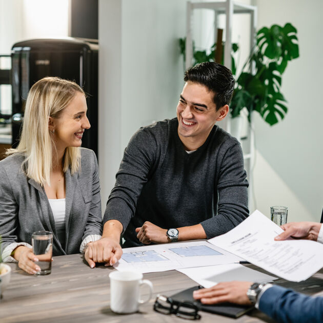 Man en vrouw kijken lachend naar elkaar, andere man kijkt naar papieren. 
