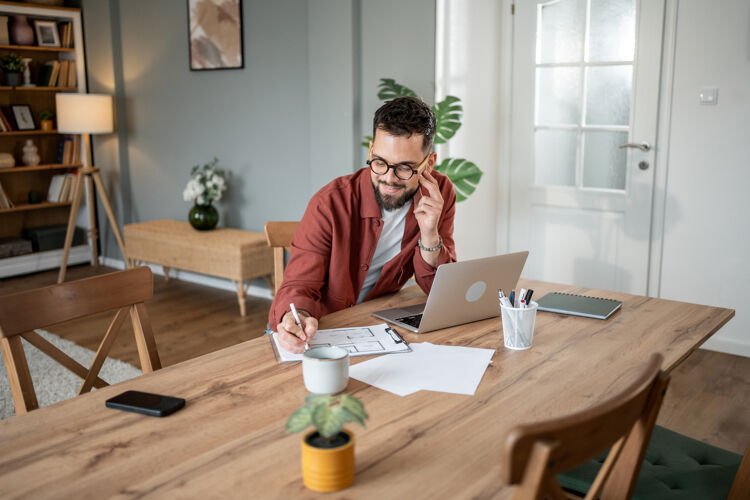 man-met-bril-achter-laptop-schrijft-op-kladblok