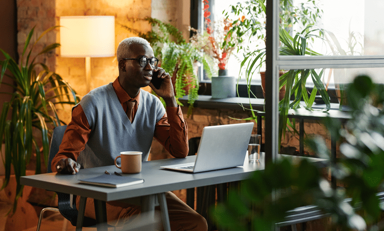 Man met bril kijkt naar laptop terwijl hij aan het bellen is 