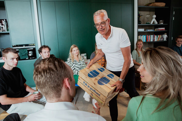 Man met wit shirt en bril houd een podium kist vast
