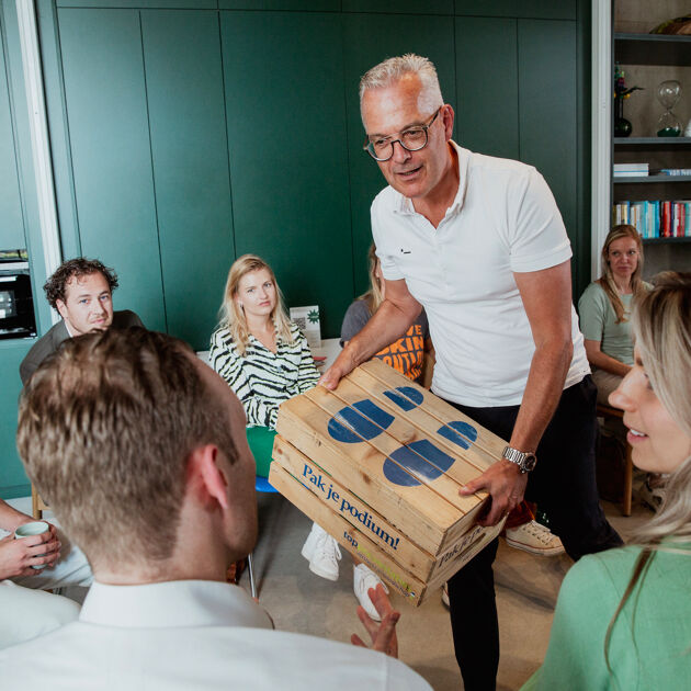 Man met wit shirt en bril houd een podium kist vast