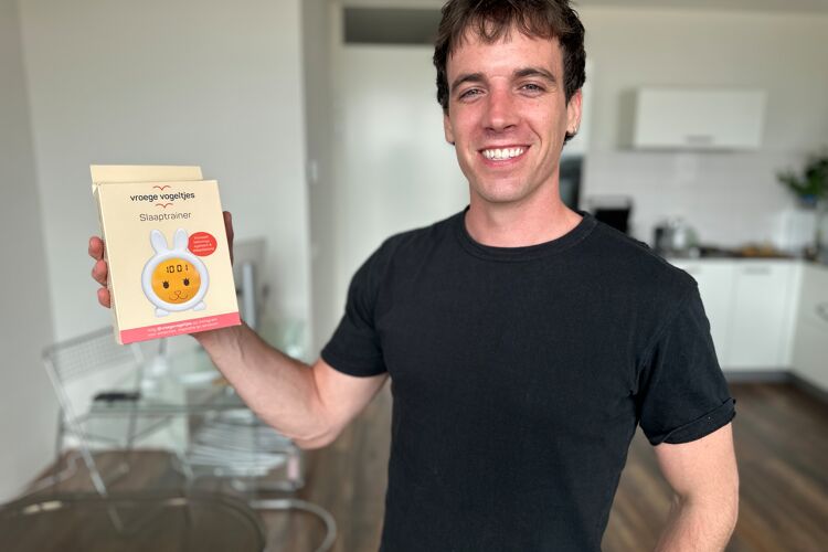 Lachende man met zwart shirt staat met een product in zijn handen. 