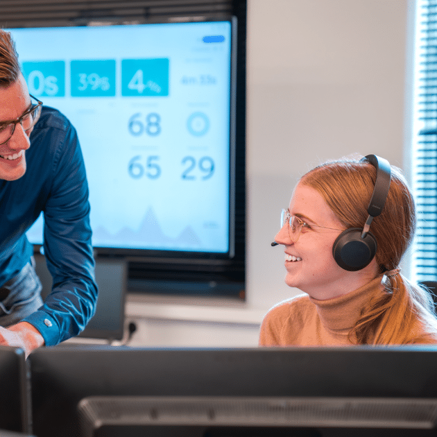 Man in blauw shirt praat tegen vrouw achter computer