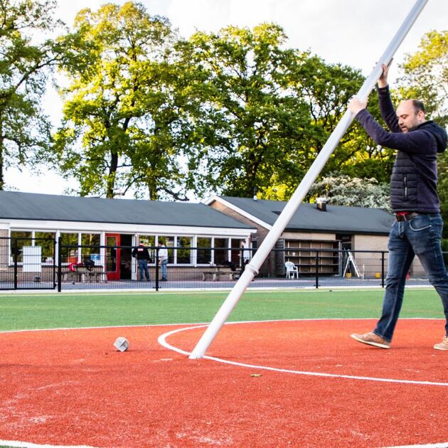 Man zet korfbal paal in de grond op een sportveld
