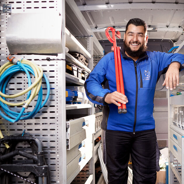 Lachende man met blauw jas staat in een werkbus met een rode tang op zijn schouders.