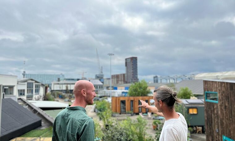 twee mannen staan buiten met bewolkt weer. Er zijn veel tiny houses op de achtergrond
