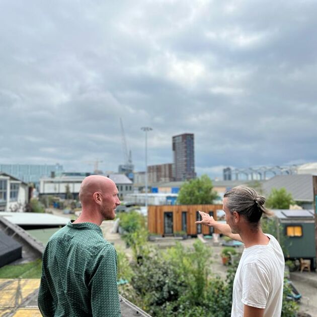 twee mannen staan buiten met bewolkt weer. Er zijn veel tiny houses op de achtergrond