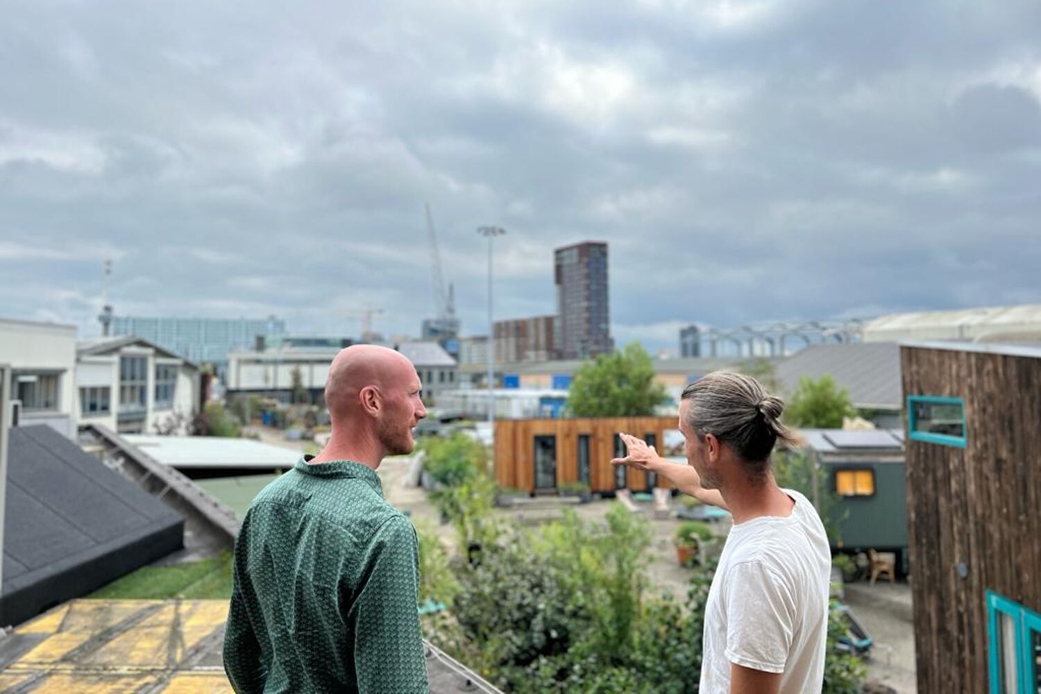 twee mannen staan buiten met bewolkt weer. Er zijn veel tiny houses op de achtergrond