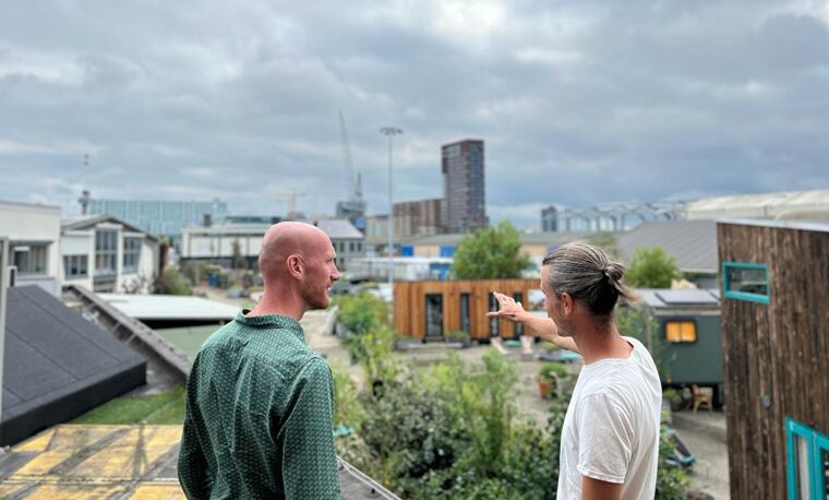 twee mannen staan buiten met bewolkt weer. Er zijn veel tiny houses op de achtergrond