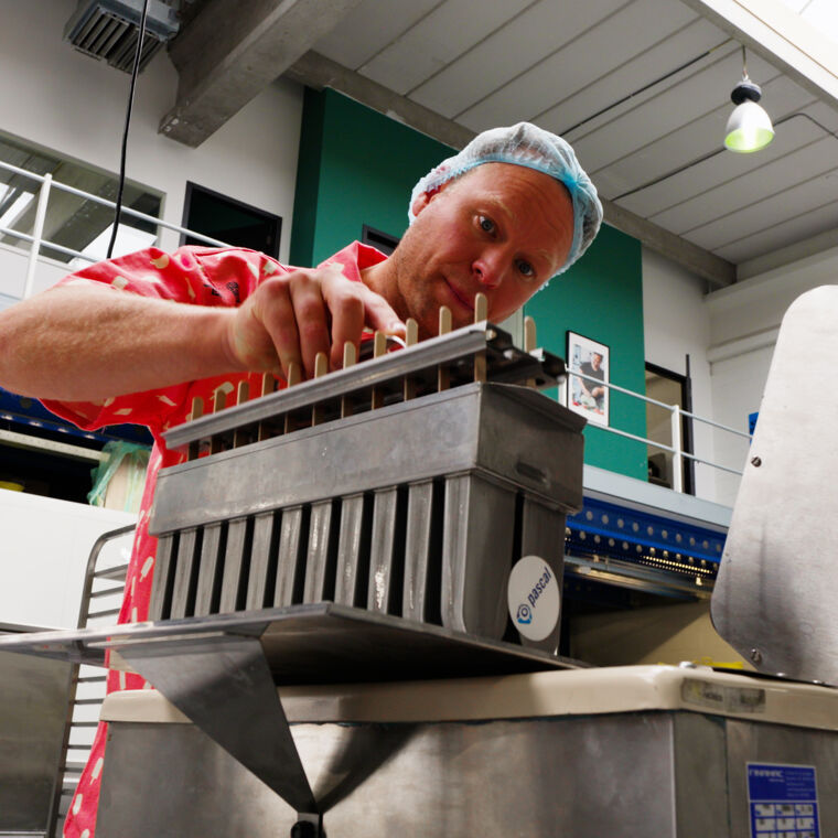 Man in roze shirt en blauw haarnetje werk met een machine dat ijsjes maakt