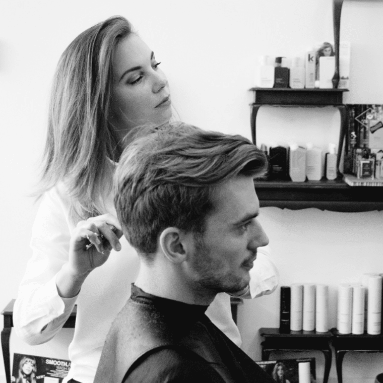 Een vrouw knipt de haren van een man, ze kijken allebei naar voren