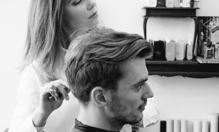 Een vrouw knipt de haren van een man, ze kijken allebei naar voren