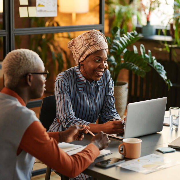 Vrouw met hoofddoek en blauwe blouse lacht zit achter laptop man ernaast