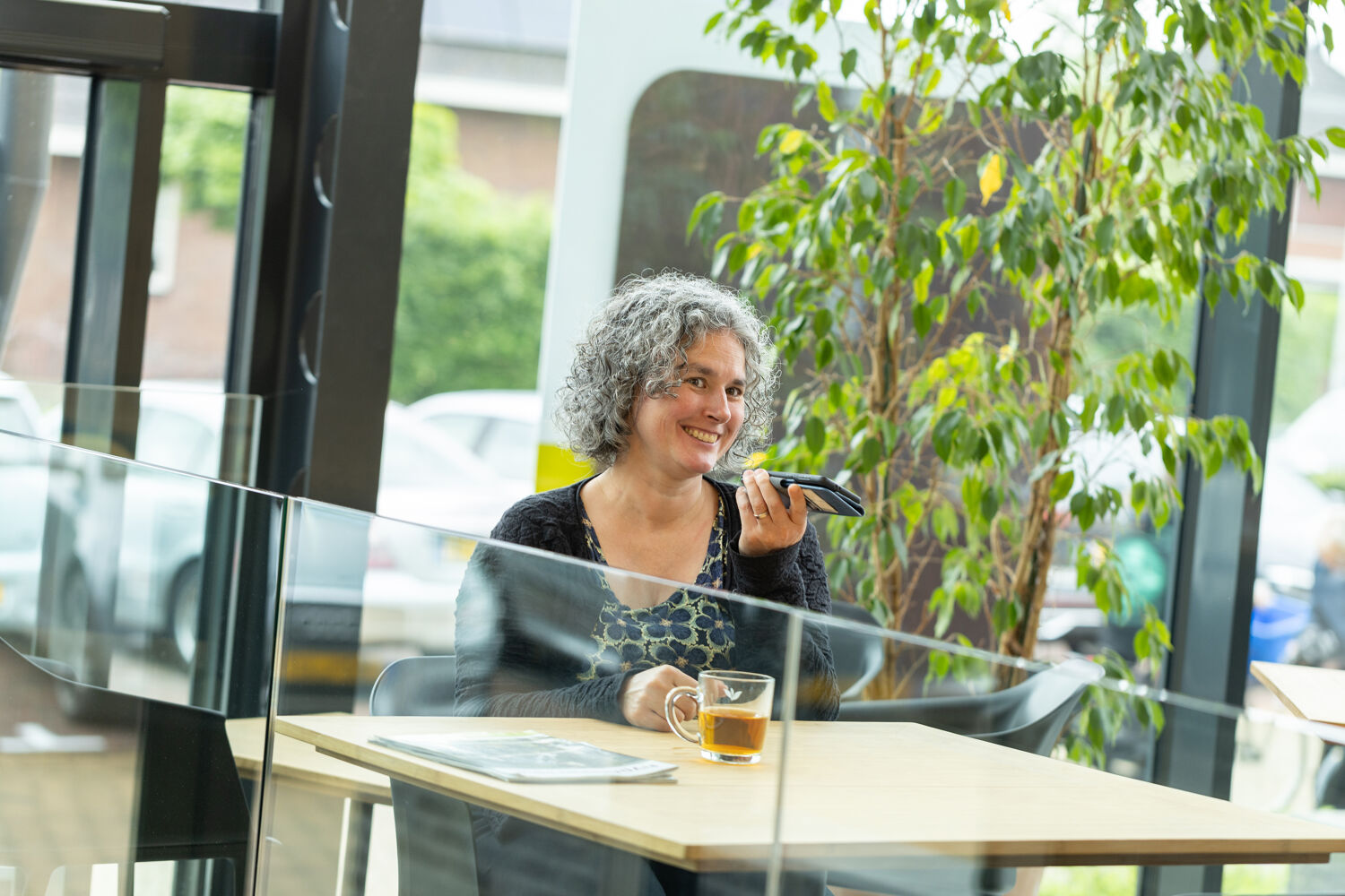 Vrouw in bloemen shirt zit aan tafel te bellen met kop thee