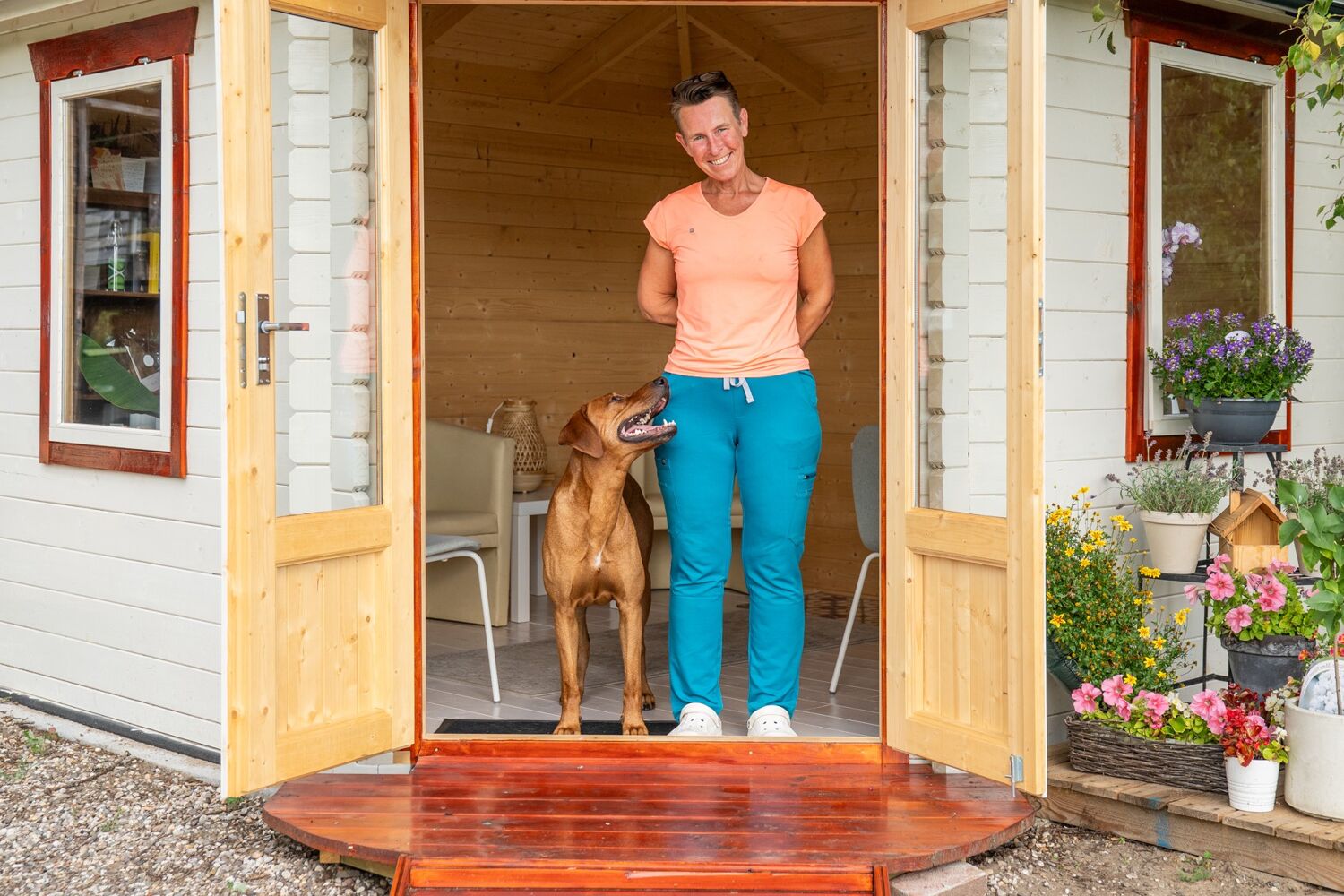 Een lachende vrouw staat in een deuropening met een bruine hond naast haar.