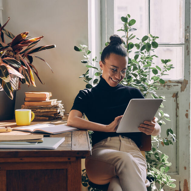 Vrouw zit achter haar bureau te lachen terwijl ze gebruik maakt van een tablet