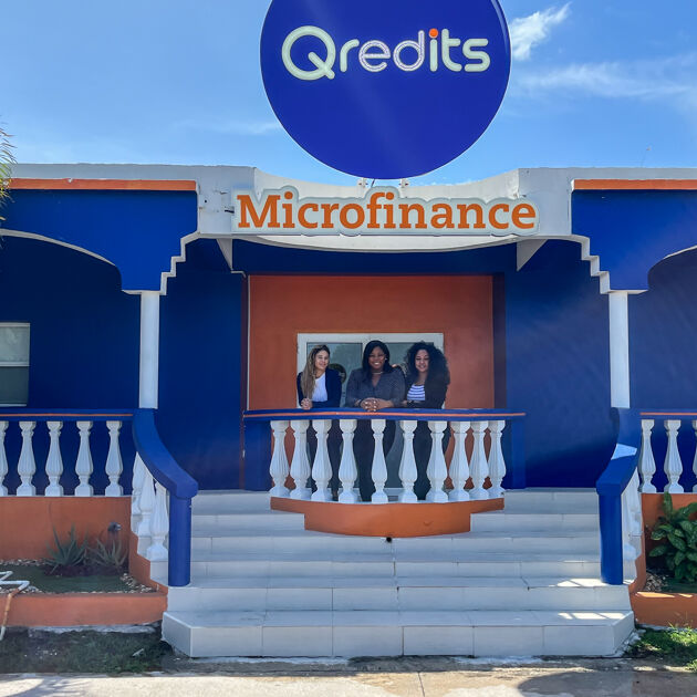 Blauw en oranje gebouw van Qredits St. Maarten met drie vrouwen vooraan