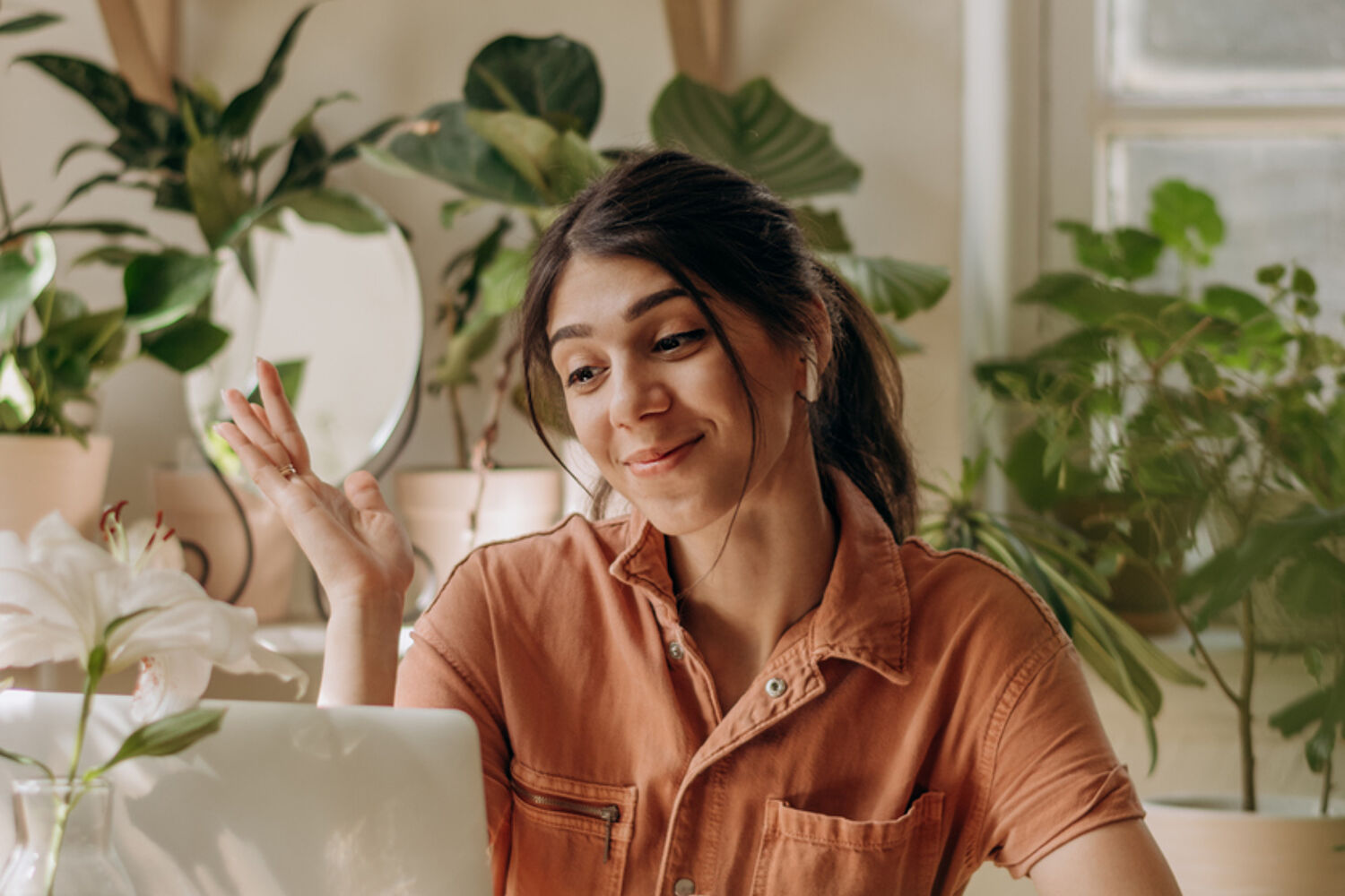 Vrouw lacht naar de laptop met veel planten