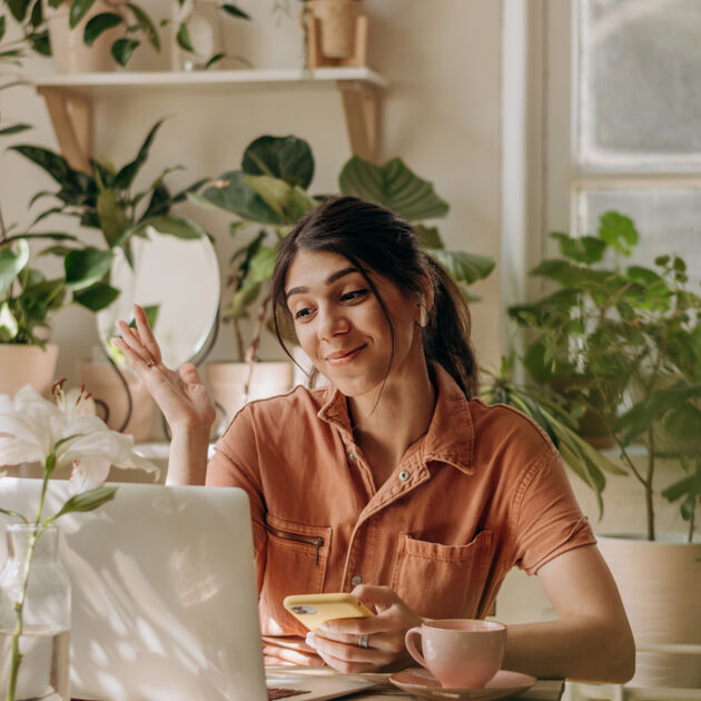Vrouw lacht naar de laptop met veel planten