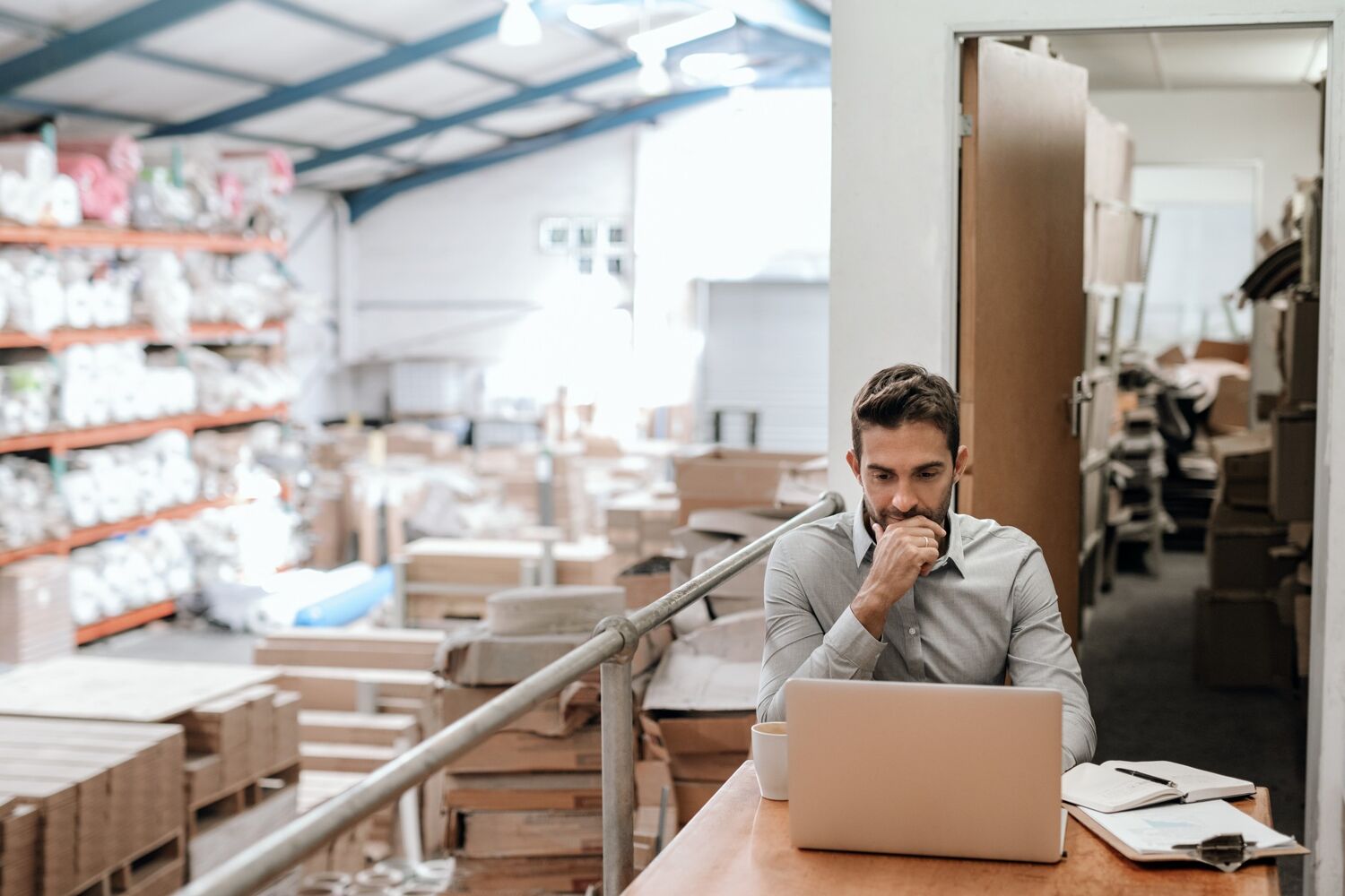 Man zit denkend met zijn hand in zijn gezicht achter een laptop in een hal. 