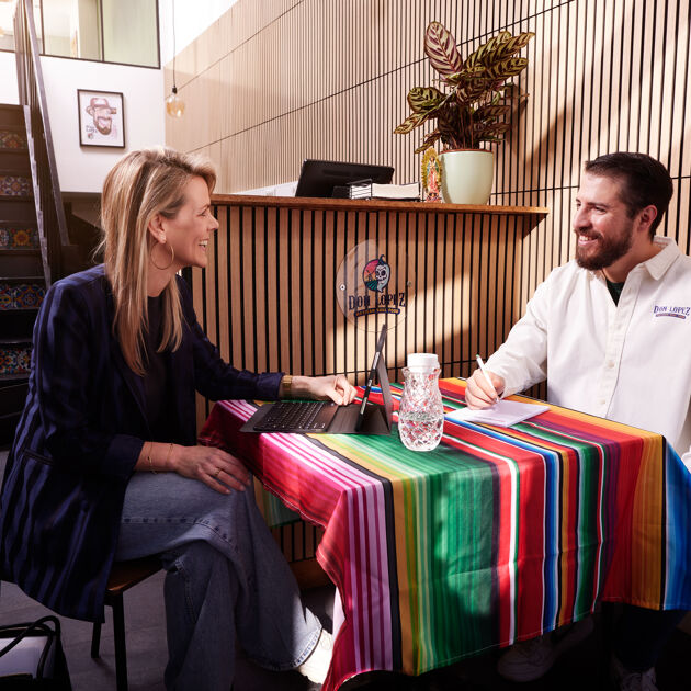Man en vrouw zitten samen aan tafel en kijken elkaar lachend aan.