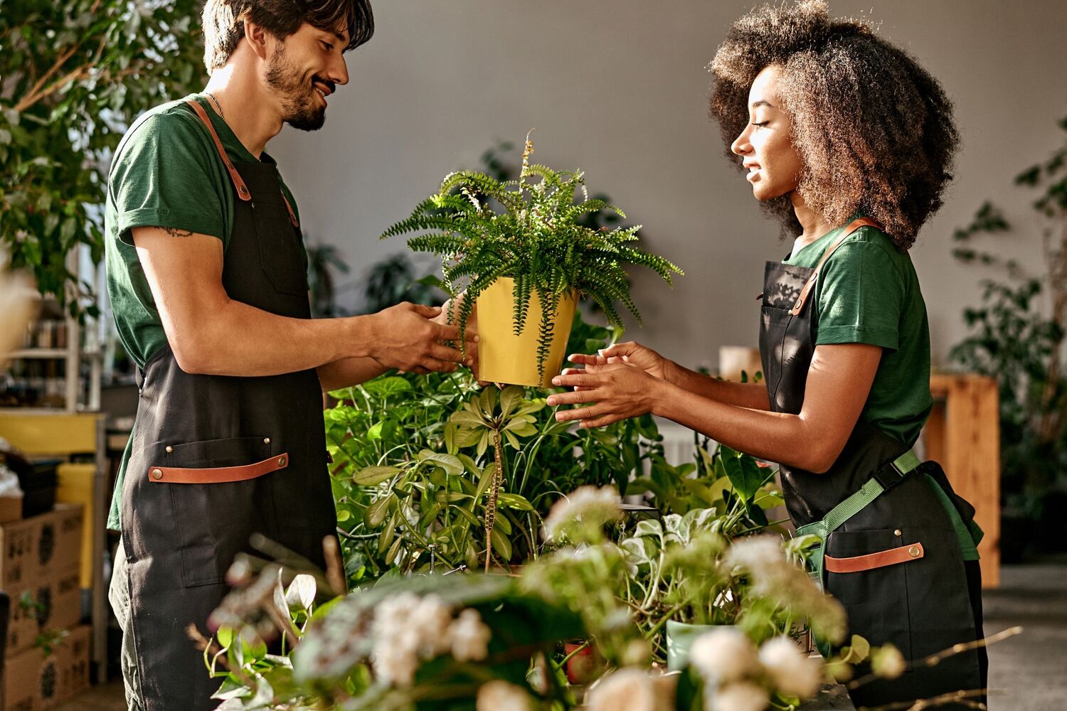 Man met schort geeft een plant aan een vrouw met schort. 