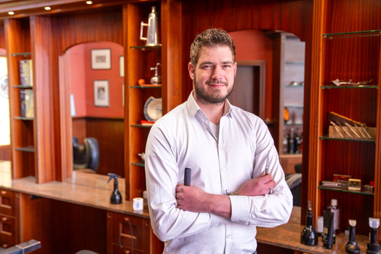 Ondernemer staat met zijn handen over elkaar in zijn eigen kapperszaak 