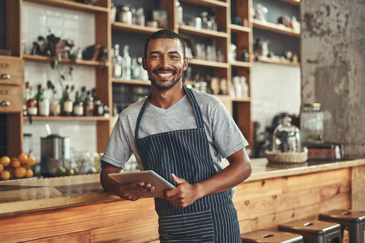 Man leunt op bar in een koffiezaak en lacht met een tablet in zijn handen
