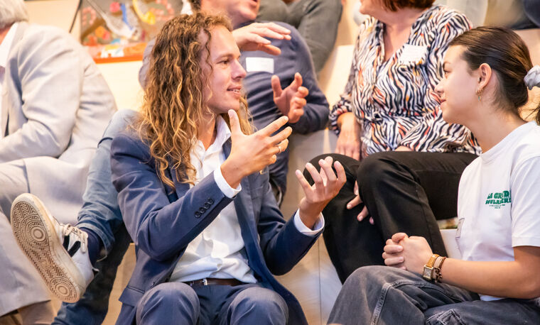 Een man met lang haar praat met een vrouw op de tribune