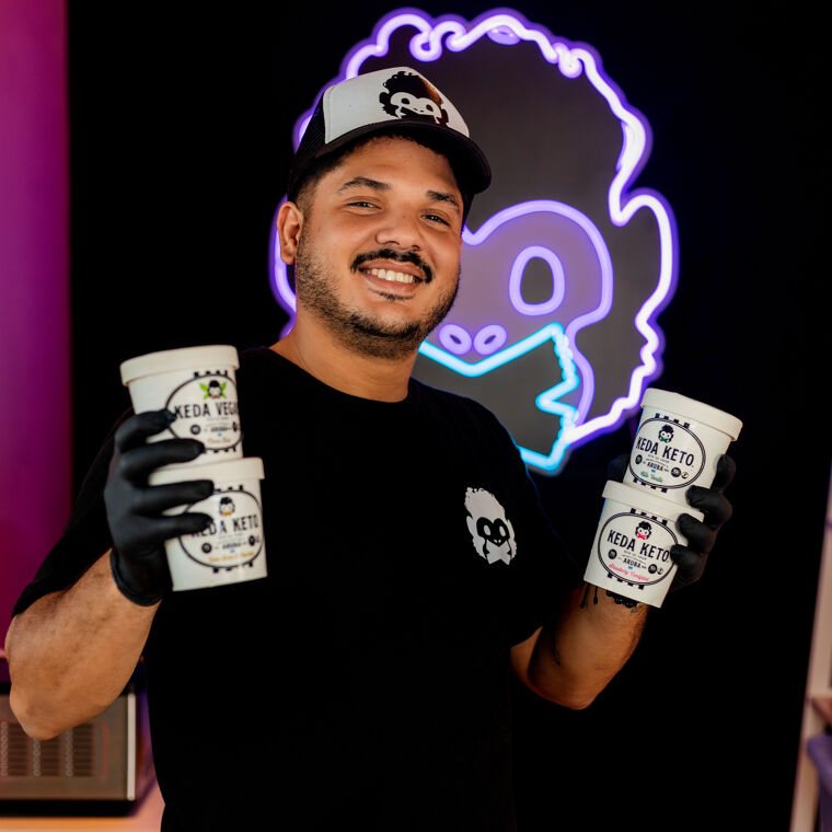 Man op Aruba in donkere kamer met pet op met neon logo achter hem.