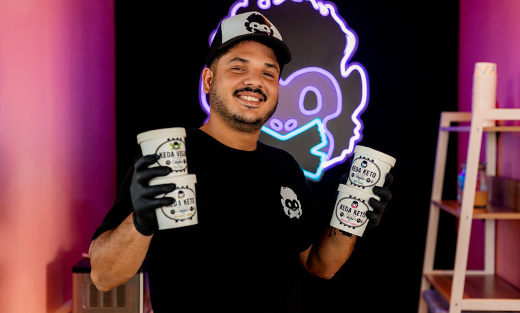 Man op Aruba in donkere kamer met pet op met neon logo achter hem.