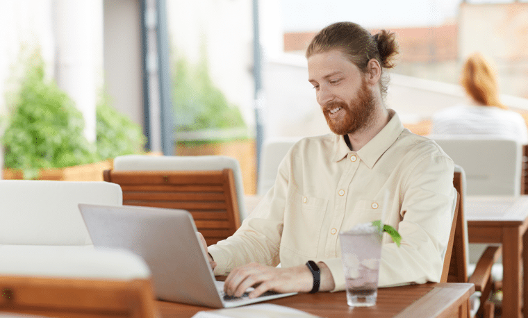 Man in licht shirt zit aan een tafel en werkt op een laptop