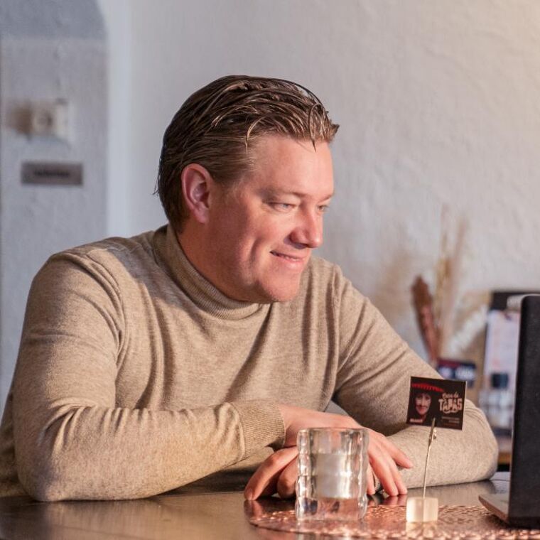 Man zit aan een tafel en kijkt naar een laptopscherm.