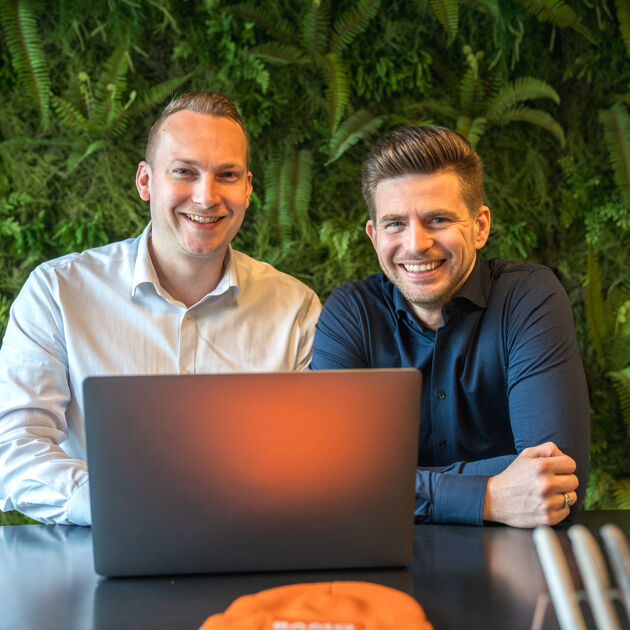 twee mannen achter de laptop voor een groene muur