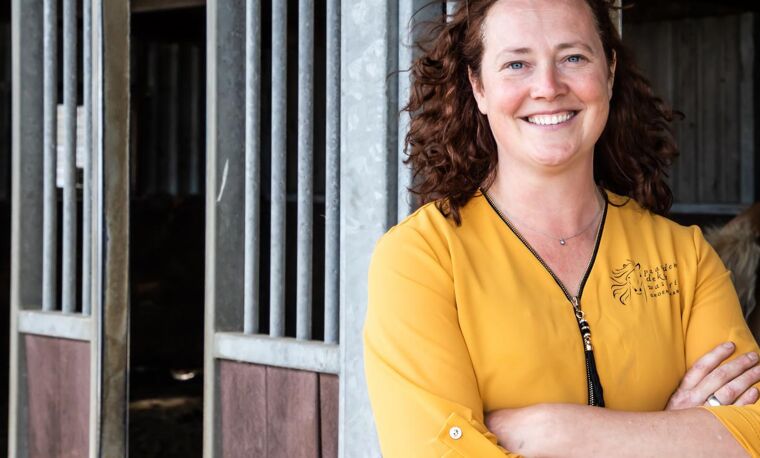 Vrouw staat voor paardenstallen en lacht.