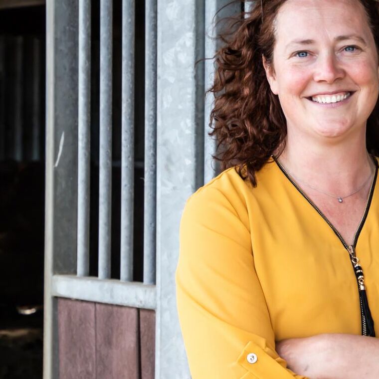 Vrouw staat voor paardenstallen en lacht.