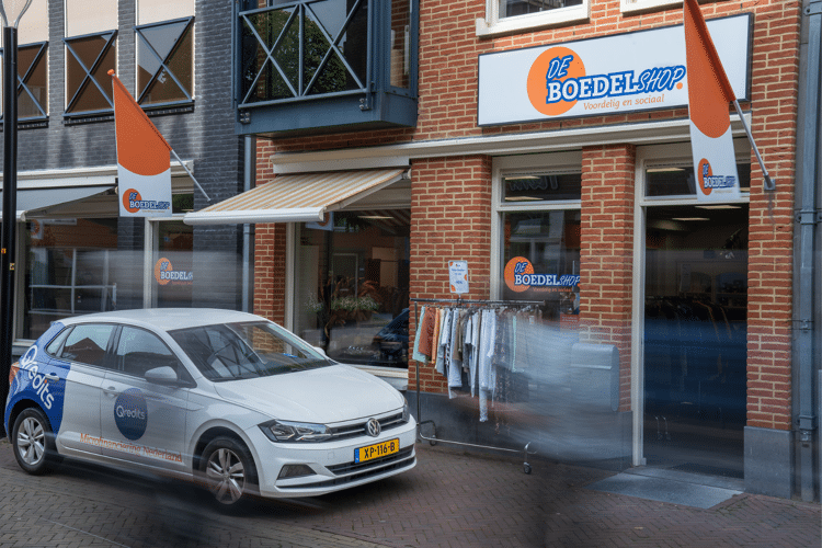 Witte auto staat voor de Boedelshop met kleding buiten