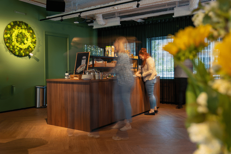 Qredits kantine met houten vloer en mensen die staan bij het eten