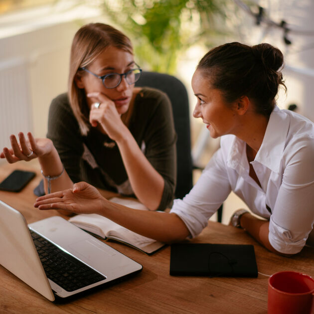 Twee vrouwen zitten aan een bureau met een laptop en zijn in overleg. 