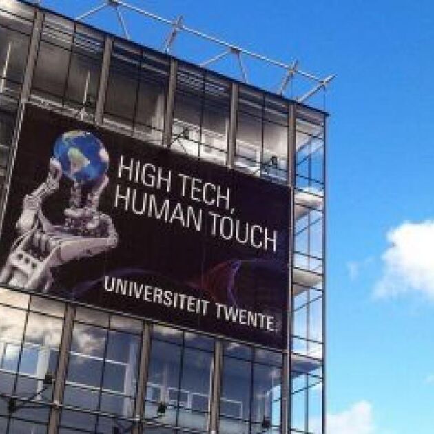 Gebouw van de Universiteit Twente met poster en blauwe lucht