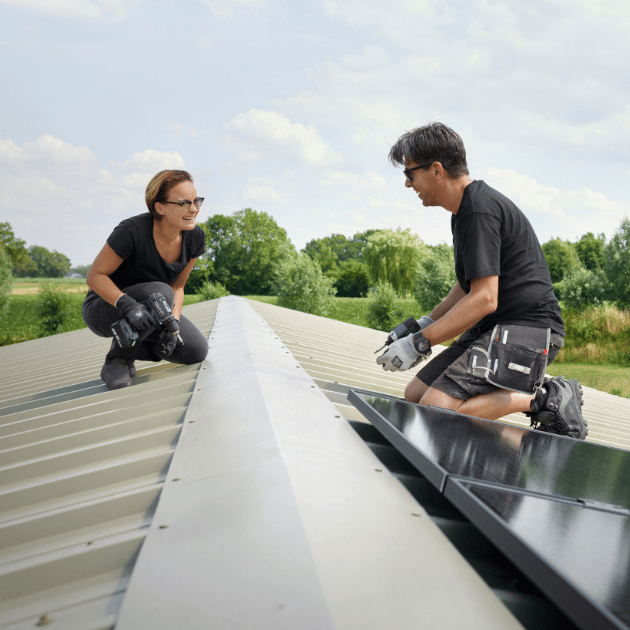 Man en vrouw leggen zonnepanelen neer op en dak